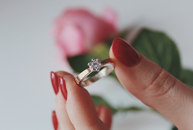 Diamantring, gehalten vor einer rosa Rose